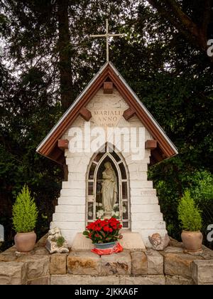 Petite chapelle rurale de pèlerinage de la Vierge Marie en pierre, Stockel, Bruxelles, Belgique. Des fleurs rouges sont placées devant Marie. Banque D'Images