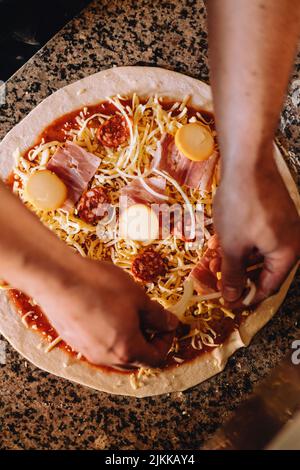 Une vue de dessus des mains ajoutant du fromage et des saucisses à la pizza Banque D'Images