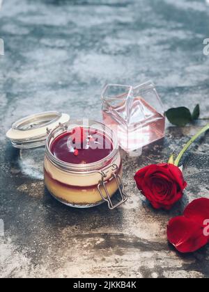 Un gros plan vertical d'un gâteau à la rose dans le pot en verre avec des roses rouges de côté Banque D'Images