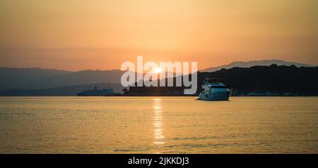 A scenic view of boats sailing against the hills covered with greenery at the sunset Stock Photo