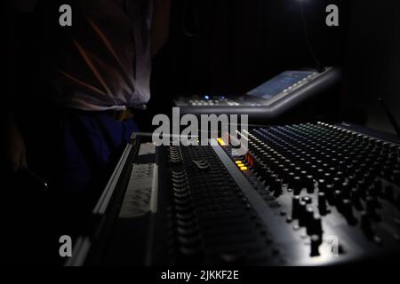 A closeup shot of a recording equipment in a dark studio, with a man standing in front of it Stock Photo