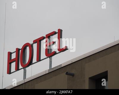 A low angle shot of a red Hotel sign on the top of a building against cloudy sky during daytime Stock Photo