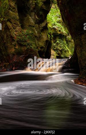 A vertical shot of a silk effect water stream flowing down through a rocky cliff Stock Photo