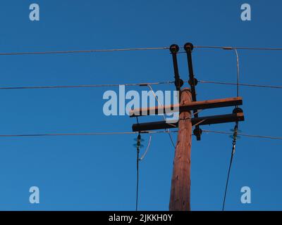 An old wooden electric pole against the cloudless sky Banque D'Images