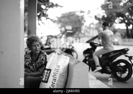 A grayscale shot of an elderly woman in the Philippines with a man riding a motorcycle behind her Stock Photo