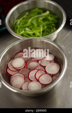 A vertical closeup shot of sliced radishes and greens in the water Stock Photo