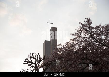 A low-angle shot through a flowering tree, on the modern white church steeple with cross on top against cloudy sky. Stock Photo