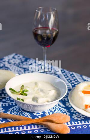 Nourriture traditionnelle géorgienne Gebjalia, fromage dans le lait et les légumes verts, espèces. Vin rouge et toile de fond bleue. Banque D'Images