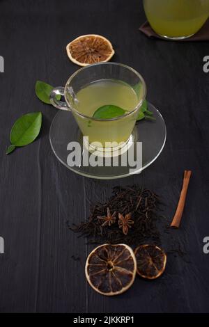 A closeup of a green tea in a transparent glass cup with dry lemons and cinnamon on a wooden surface Banque D'Images