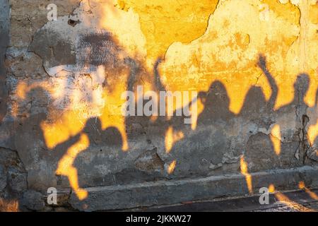 Des ombres de dansant sur un vieux mur au coucher du soleil. Groupe d'ombres humaines sur l'arrière-plan de la paroi en pierre. Banque D'Images