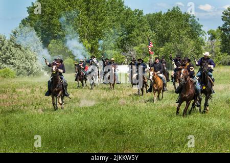 Les soldats AMÉRICAINS vêtus d'uniformes de cavalerie se portent à cheval tout en tirant six coups de feu pendant la reconstitution de Little Bighorn, également connue sous le nom de Custer's Last Banque D'Images