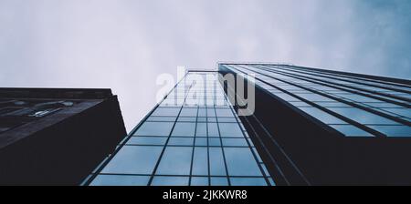 A low-angle shot of a blue glass facade of a high-rise building ascending to the foggy clouds Banque D'Images