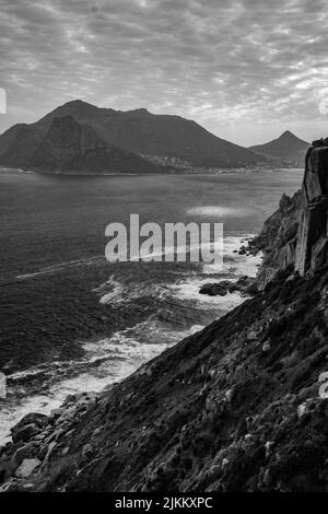 Un cliché vertical des vagues de l'océan s'écrasant contre les falaises rocheuses sous un ciel nuageux en niveaux de gris Banque D'Images