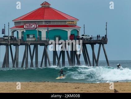 A scenic view of a Ruby's diner on a pier above people surfing at Huntington Beach, California Stock Photo