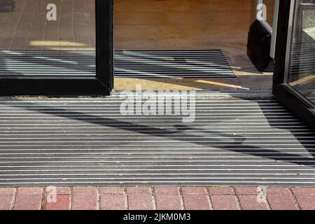 entrée à l'hôtel depuis une plieuse sur un tapis de sol par une porte en verre, vue extérieure un bâtiment en gros plan par temps sec ensoleillé personne. Banque D'Images