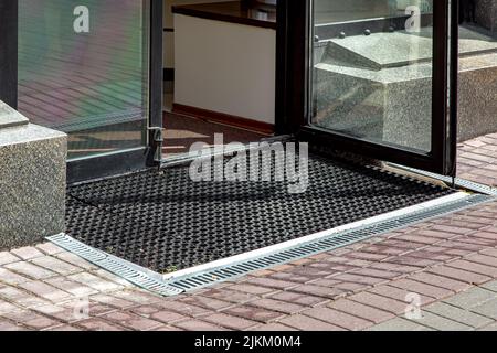 descente à l'entrée du magasin depuis le trottoir piétonnier avec tapis de sol en caoutchouc avec réseau d'évacuation des tempêtes grises, façade en granit de l'extérieur en pierre du bâtiment Banque D'Images