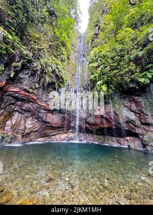 A low angle shot of a waterfall flowing down the rocks covered with greenery Stock Photo