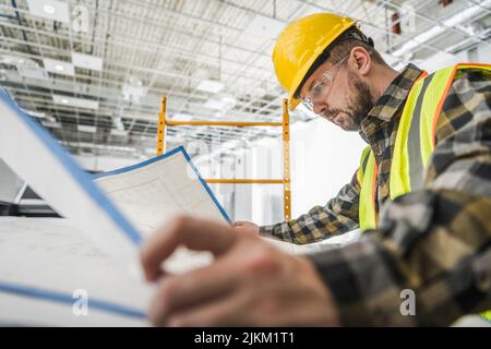 Développement de bâtiments commerciaux.Superviseur de chantier de construction caucasien dans ses années 30 en train de jeter un coup d'œil rapide sur un plan de construction du bâtiment. Banque D'Images