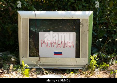 Une vieille télévision cassée et du papier de carton avec de la propagande textuelle et un drapeau russe peint et la télévision elle-même se tient dans la forêt sur l'herbe en Ukraine. Banque D'Images