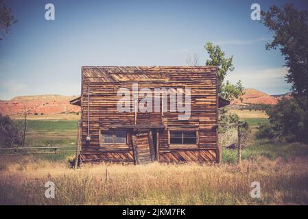 An old wooden hut with a broken door isolated in the field under the blue sky Stock Photo