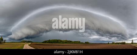 A panoramic shot of gray stormy clouds over green beautiful farm Banque D'Images
