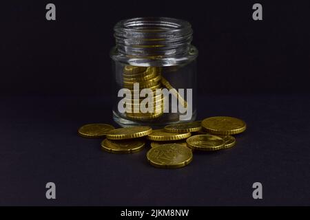 Gros plan d'un pot en verre rempli de pièces de monnaie et de pile de pièces de monnaie autour d'elle sur un fond gris Banque D'Images