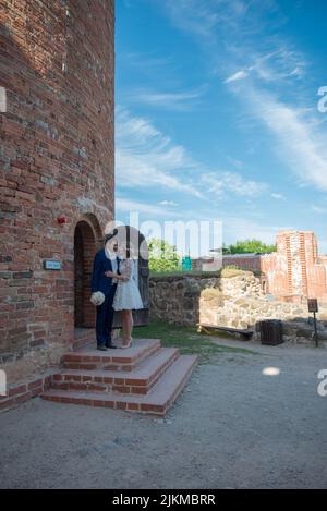 Un couple de jeunes mariés caucasiens s'embrassant debout sur la porte latérale d'une ancienne église fortifiée en brique Banque D'Images