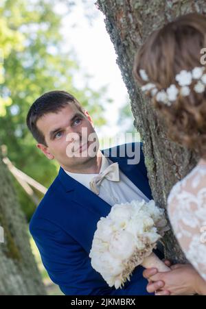 Un cliché vertical de jeunes mariés caucasiens se regardant les uns les autres tout en se tenant à côté d'un arbre Banque D'Images