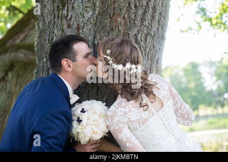 Un gros plan de jeunes mariés caucasiens se regardant les uns les autres tout en se tenant à côté d'un arbre Banque D'Images