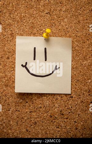 A vertical shot of a smiley face on an attached sticky note Stock Photo