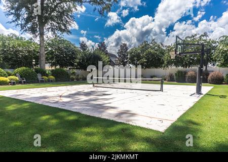 Une grande cour avec de l'herbe verte et un terrain de basket-ball qui a été fait dans un terrain de pickleball à la maison Banque D'Images