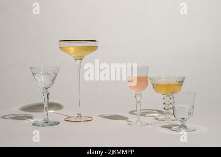 disposition de différents verres à cocktail sur fond blanc avec du liquide rose et or Banque D'Images