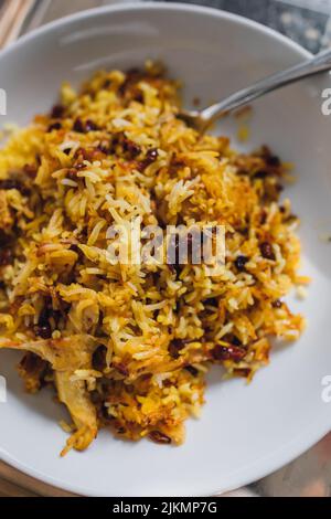 Zereshk Polo ba morgh, serving of Persian Saffron basmati rice dish with barberries and chicken in white bowl with fork Stock Photo