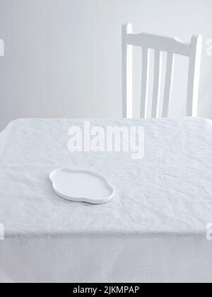 A Table with plates and a chair on a white minimalistic setting Stock Photo