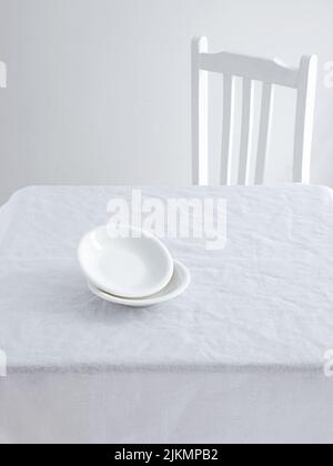 A Table with plates and a chair on a white minimalistic setting Stock Photo