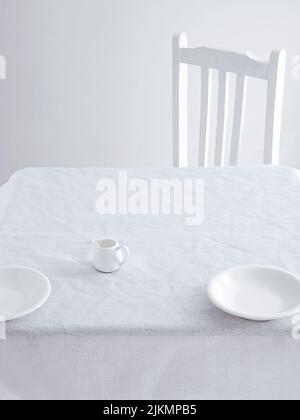 A Small coffee cup and plates on a table and a chair on a white minimalistic setting Stock Photo