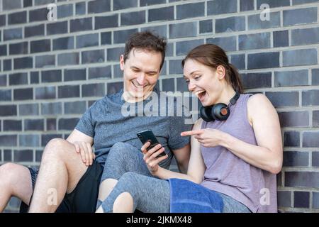 le jeune couple prend une pause après l'entraînement de fitness et regarde le smartphone Banque D'Images