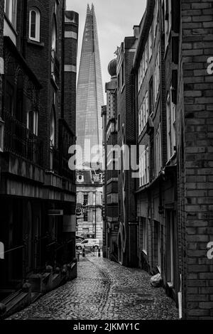 A grayscale shot of a London alleyway with a shard in the background in London, UK Stock Photo