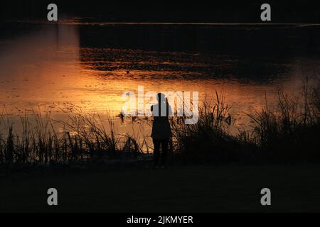 The silhouette of a young photographer enjoying and taking pictures of a beautiful seascape at sunset Stock Photo