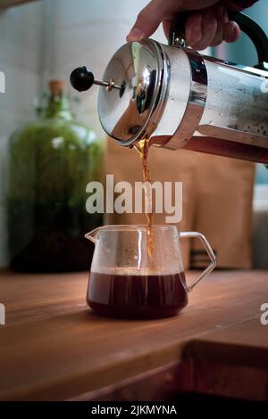 A vertical shot of a male pouring coffee from French press into the glass cup Banque D'Images
