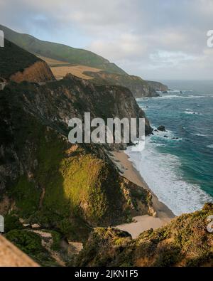 A vertical high angle shot of the ocean waves hitting the coast with cliffs Stock Photo