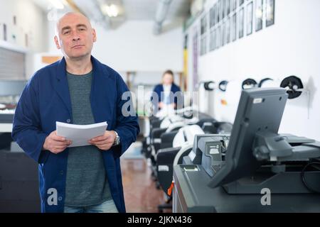 Portrait d'un employé de la maison d'impression avec pile de papier dans ses mains Banque D'Images