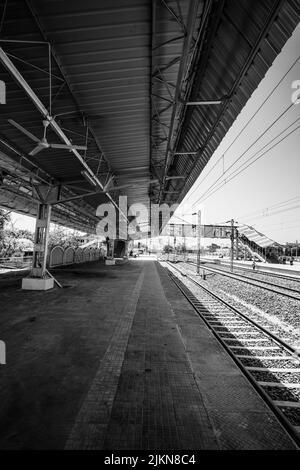 A vertical shot of an empty train station on a sunny day in grayscale Stock Photo