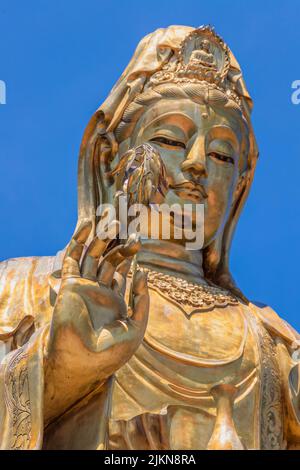 A vertical closeup shot of a golden Buddha statue against a clear cloudless sky Stock Photo