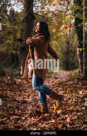 Femme dansant joyeusement sur un chemin couvert de feuilles sèches en automne. Banque D'Images