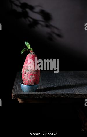 A vertical closeup of a single radish in a tiny bowl on a wooden table Banque D'Images
