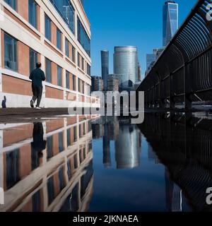 a ground-level shot of New York skyline reflected in a pond of water on a street, a man jogging past Stock Photo