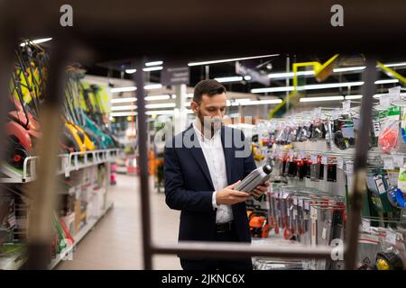 un homme dans un costume d'affaires choisit l'huile moteur pour une tondeuse à gazon Banque D'Images