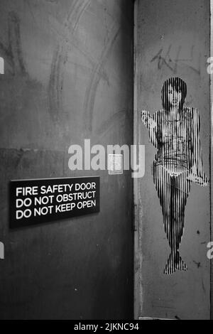 A vertical grayscale shot of street art adjacent to a building fire exit. New Zeland. Stock Photo