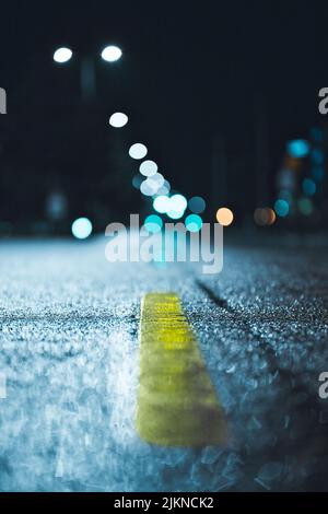 A yellow traffic line on wet asphalt at night against bokeh lights Stock Photo